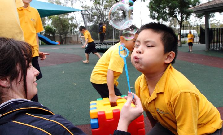 A student blows bubbles with a teacher within the playground at Western Sydney School